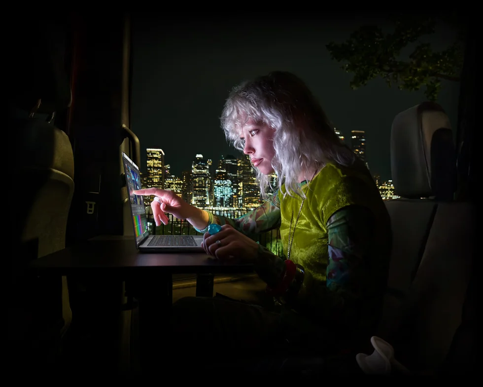 Žena pracuje večer s MacBookem Pro u okna s výhledem na město